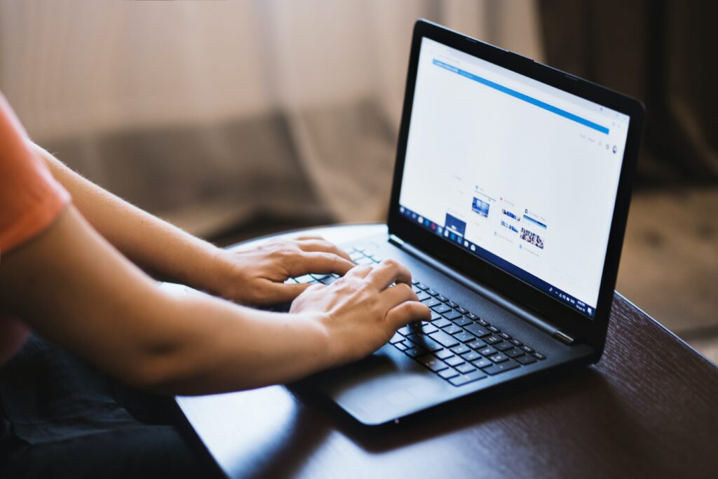 Human typing on a laptop that is sat on a desk.